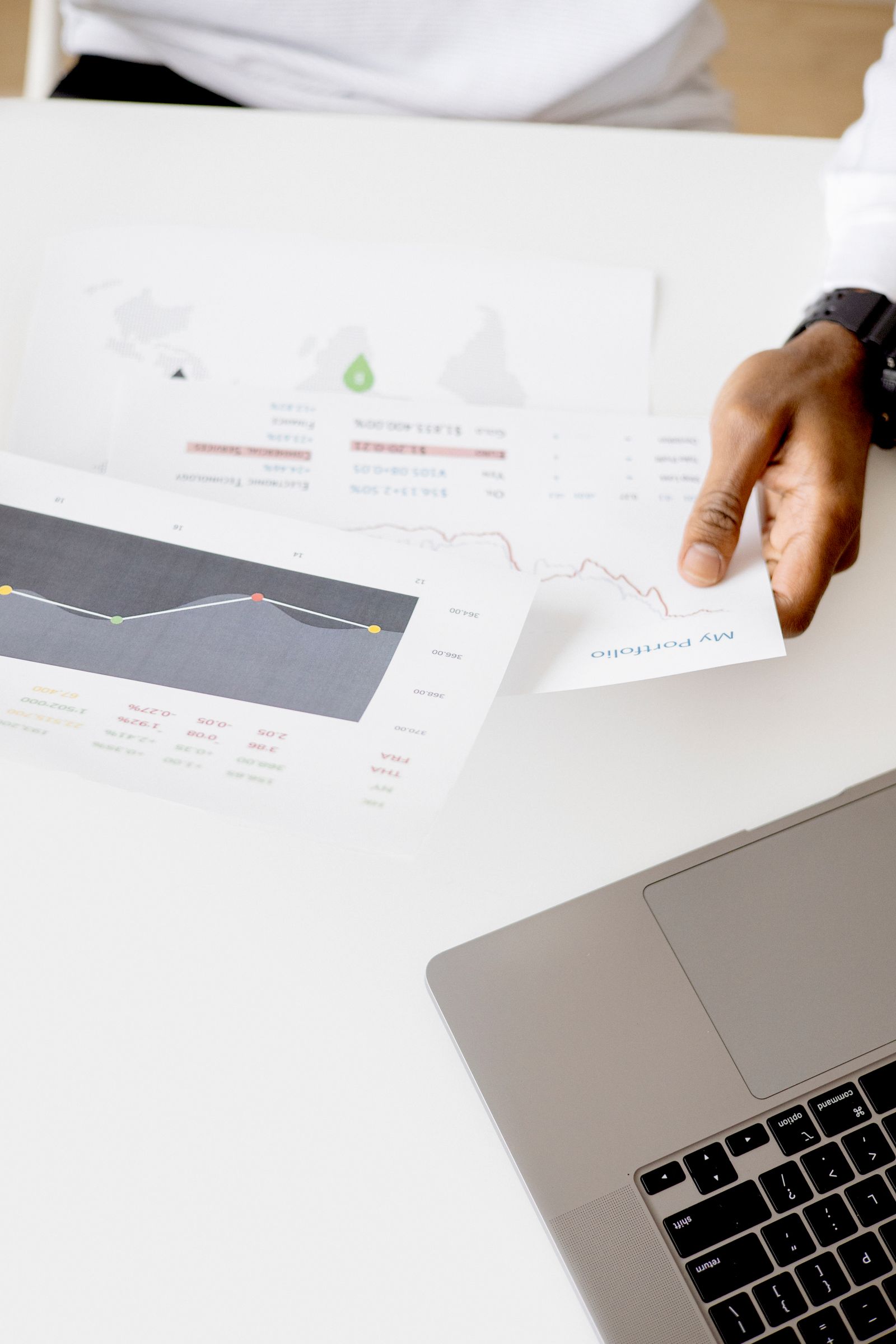 Mão segurando relatório com gráficos ao lado de um notebook sobre uma mesa de trabalho